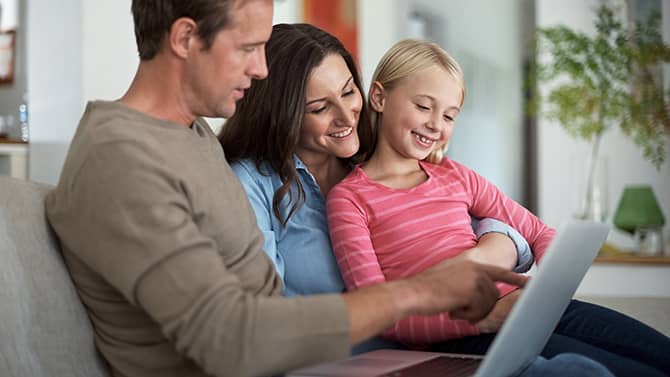 Un blog privado puede evitar que extraños se enteren de detalles personales sobre su familia. La imagen muestra dos padres y su hija sentados en un sofá, mirando una tableta juntos.